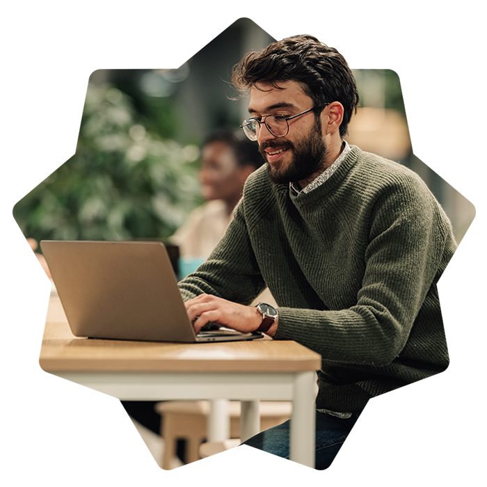 Uomo con la barba e occhiali sorridente mentre usa il laptop in ufficio