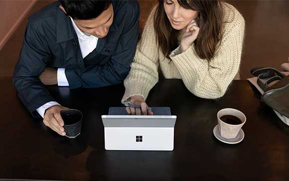A woman using Microsoft Surface Go 2 with a man beside him looking on the device